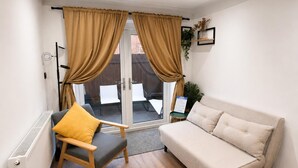 A room with a sofa, a chair, a radiator, a window with curtains, and a small table with a plant. - Chester Charm - Spacious 3 Bedroom House (Chester)
