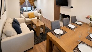 A modern living room with a sofa, coffee table, and dining area with chairs and a table set for two. - Chester Charm - Spacious 3 Bedroom House (Chester)