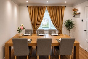 A dining area with a wooden table, grey upholstered chairs, and a window with curtains. - The Cloud House Spa Retreat Hoole (Chester)