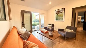 Una sala de estar con un sofá, sillones, una mesa de centro y una puerta que da al exterior.