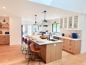 A modern kitchen with a central island, bar stools, pendant lighting, and a large window. - Ojai Valley Luxury Hillside Estate (Ojai)
