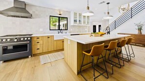 A modern kitchen with a central island, bar stools, a stove, and a staircase. - Ojai Valley Luxury Hillside Estate (Ojai)
