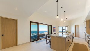 Eine moderne Küche mit einer großen Kochinsel, einem Essbereich und Blick aufs Meer.