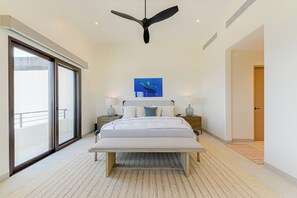 Une chambre à coucher avec un lit, un ventilateur de plafond, une grande fenêtre et un tableau accroché au mur.