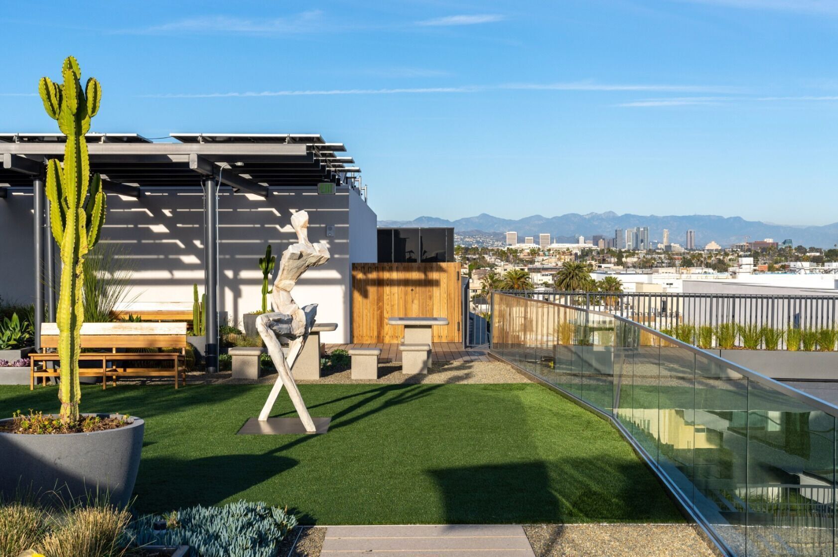 Une terrasse sur le toit, avec un revêtement d’herbe artificielle, un cactus, un banc en bois, une sculpture et une vue sur le paysage urbain.