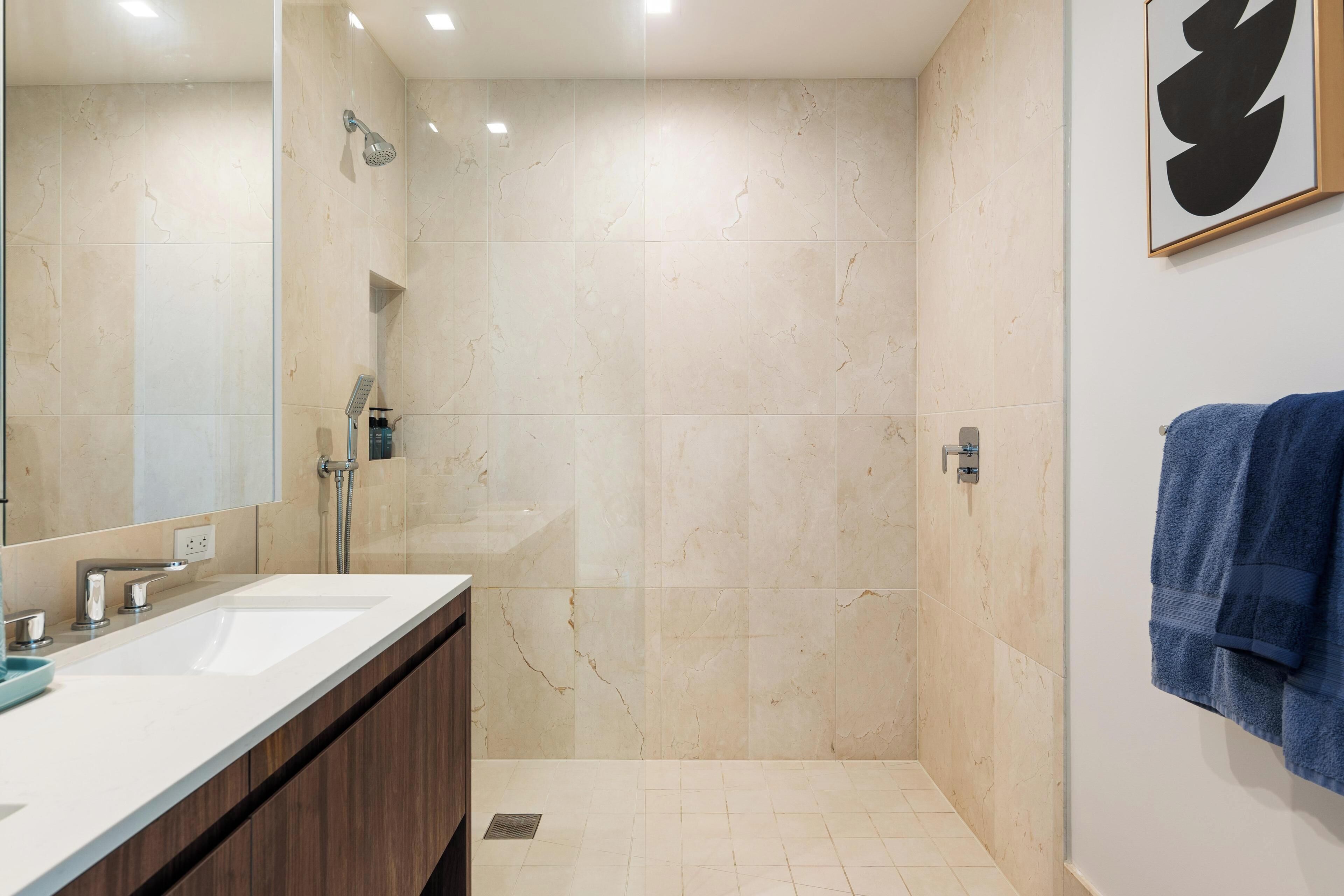 A modern bathroom with a large mirror, a shower, and a sink.