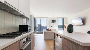 A modern kitchen with a gas stove, oven, and microwave. There is a dining area with a table and chairs, and a large window offering a view of the city. - The Rose Quartz' Rooftop Pool, Luxury 2BR 2BA Santa Monica Beach, Walk To Pier (Santa Monica)