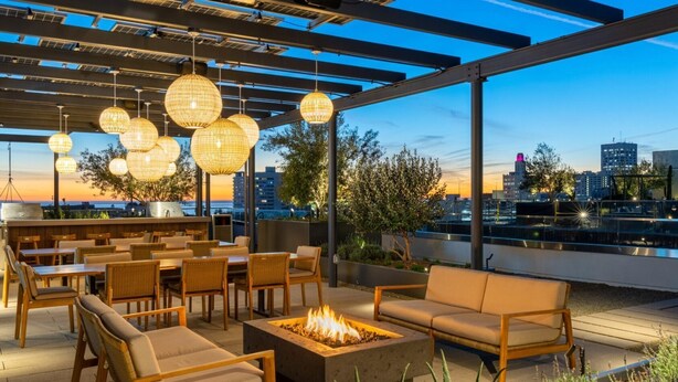 An outdoor seating area with wicker furniture, a fire pit, and hanging lights. - The Rose Quartz' Rooftop Pool, Luxury 2BR 2BA Santa Monica Beach, Walk To Pier (Santa Monica)