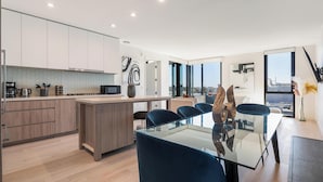 A modern kitchen with a central island, a dining area with a glass table, and a view of the city through large windows. - The Rose Quartz' Rooftop Pool, Luxury 2BR 2BA Santa Monica Beach, Walk To Pier (Santa Monica)