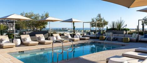 A poolside area with lounge chairs, umbrellas, and a view of the sea.