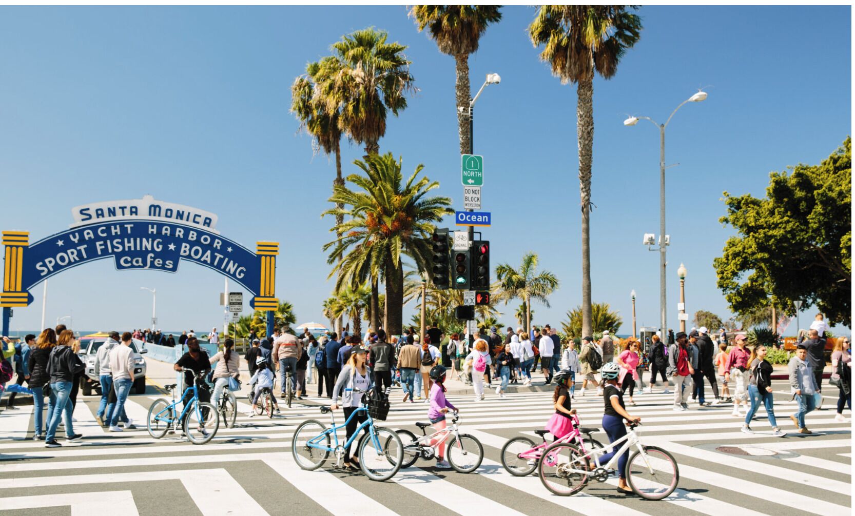 Eine belebte Straße mit einem Schild für den Santa Monica Yacht Harbor und Cafés.