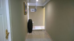 A hallway with a tiled floor, a door with a gold handle, a black vase, and a white air conditioning unit on the wall.