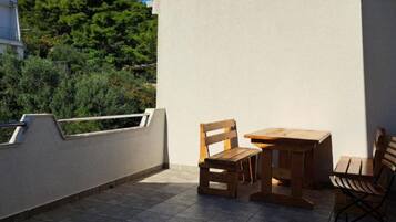 Un balcón con una mesa y sillas de madera, una pared blanca y vistas a una ladera verde.
