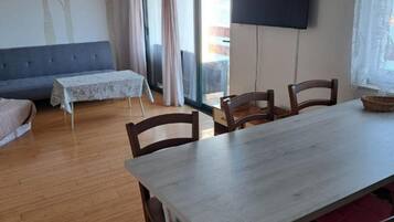 Un comedor con una mesa y sillas, un sofá, una mesita con mantel estampado y un televisor grande montado en la pared.