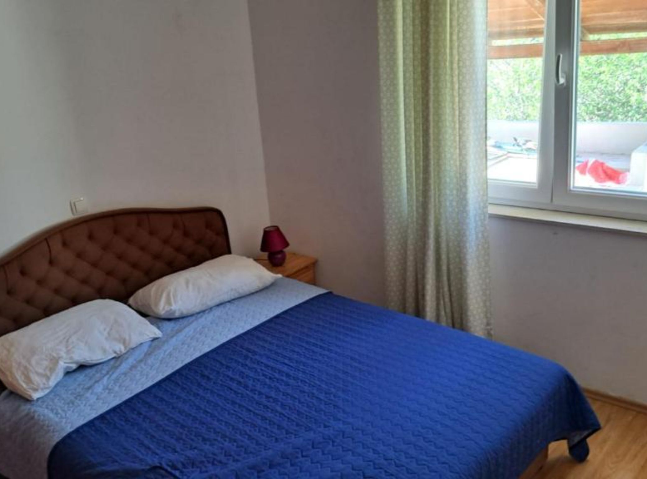 Une chambre à coucher avec un lit, des oreillers, une table de chevet, une lampe et une fenêtre avec des rideaux.