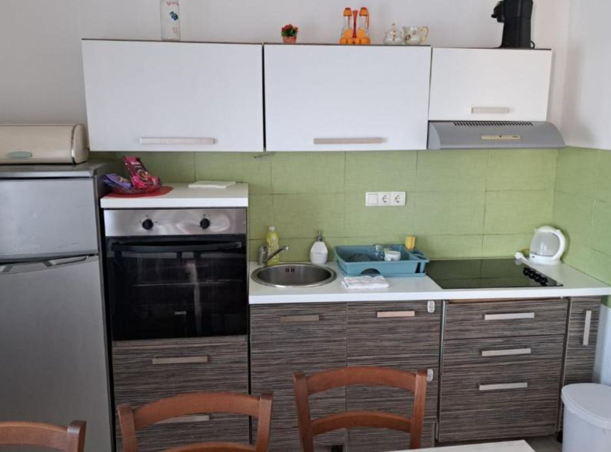 A compact kitchen with a refrigerator, oven, sink, and a microwave on the countertop.