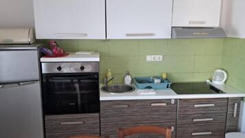 A compact kitchen with a refrigerator, oven, sink, and a microwave on the countertop.