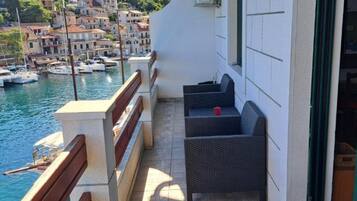Un balcon agrémenté de meubles en osier, une vue sur les bateaux et une colline parsemée de bâtiments.