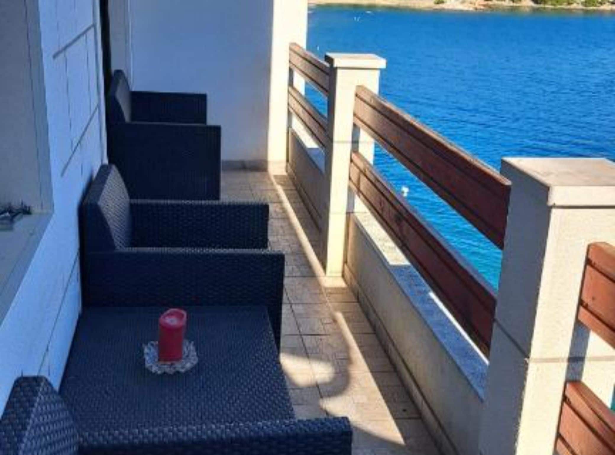 Varanda com vista para o mar, degraus que levam à porta e uma mesa pequena com uma vela.