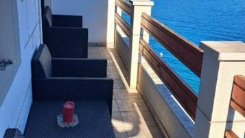 Varanda com vista para o mar, degraus que levam à porta e uma mesa pequena com uma vela.