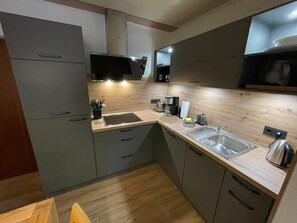 A modern kitchen with grey cabinets, a wooden countertop, a built-in oven, and a stainless steel sink. - Vacation home Kompass - Apartment Kompass (Wittmund)