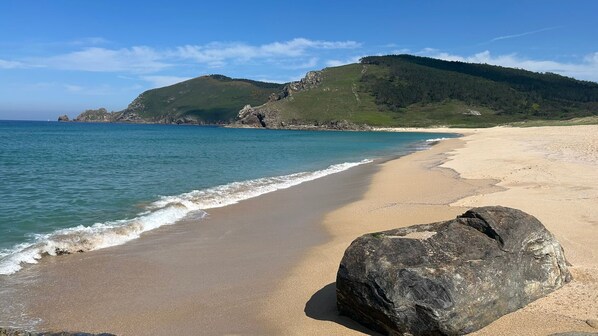 A beach with a large rock in the foreground, a sandy shore, and a hill with trees in the background. - Casa Frutales - Charming country house with orchard near the beach in Finisterre (As escaselas)