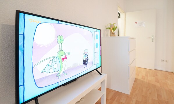 A television displaying a cartoon, a white cabinet, and a wooden floor. - Convenient 1-room apartment with good transportation links, near the university hospital (Magdeburg)