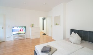 A modern bedroom with a bed, a TV, and a hallway leading to a bathroom. - Convenient 1-room apartment with good transportation links, near the university hospital (Magdeburg)