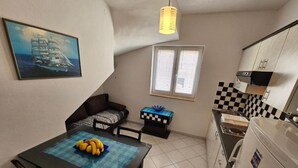 Eine kompakte Küche mit Essbereich, einer kleinen Sitzecke und einem Fenster mit Jalousien.