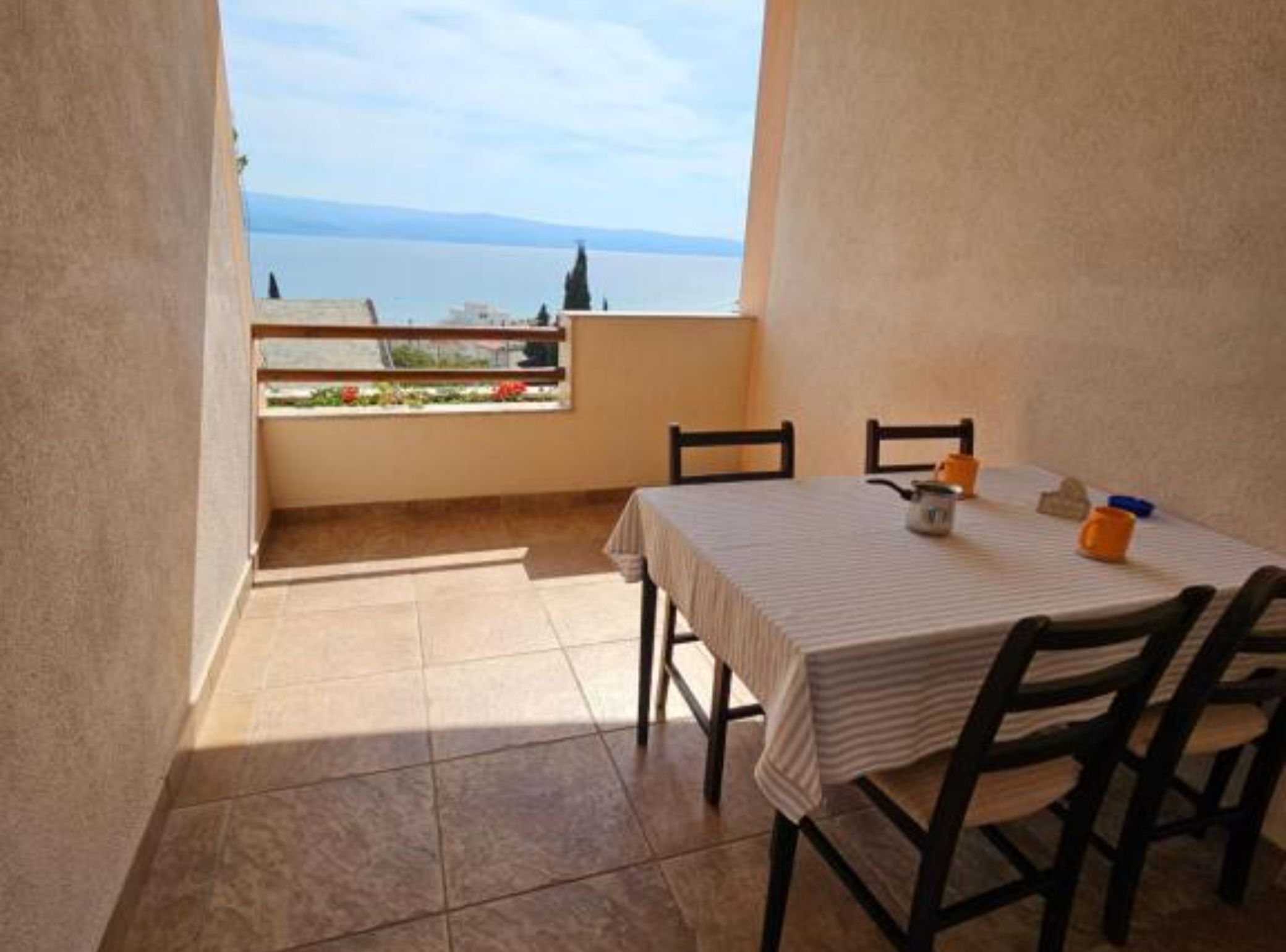 Ein Balkon mit Tisch und Stühlen, der auf ein Gewässer und ferne Berge blickt.
