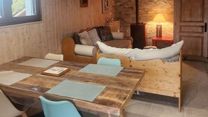 A cozy living room with a wooden dining table, blue chairs, a sofa, and a stone wall.