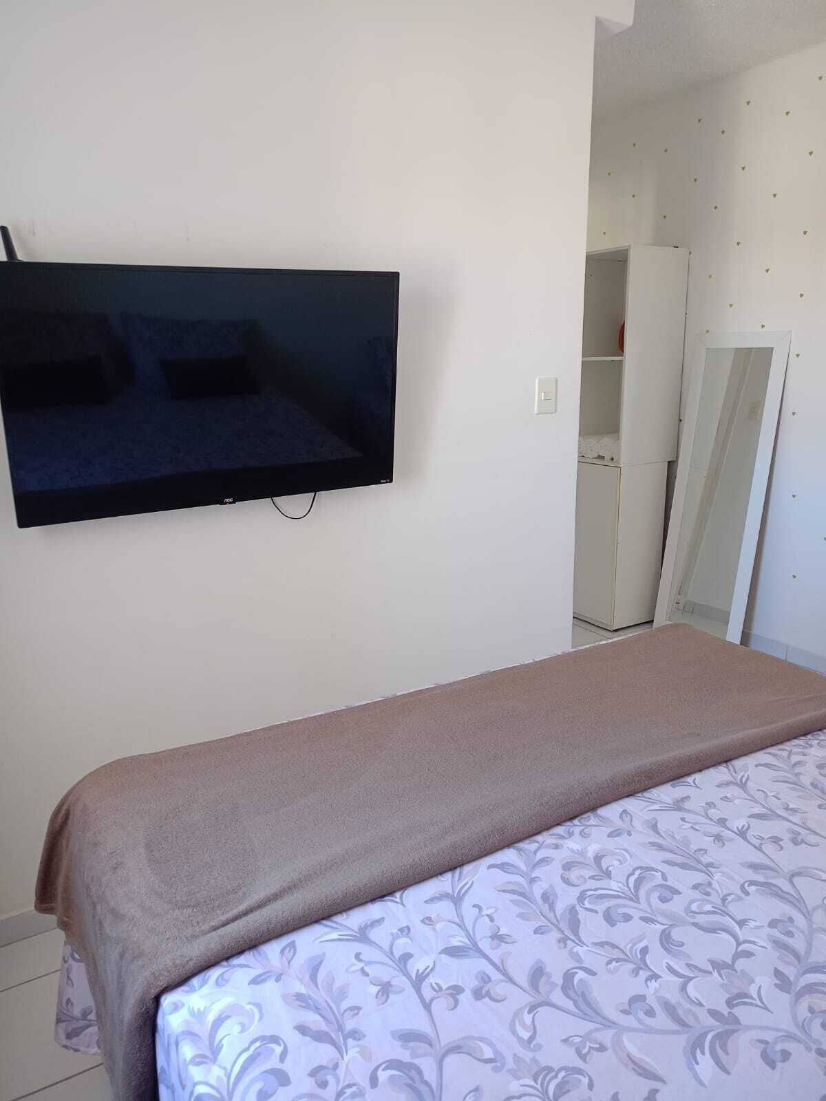 A bedroom with a bed, a television mounted on the wall, and a wardrobe.