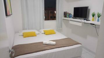 Quarto de hotel bem arrumado com cama, televisão e janela com cortinas.