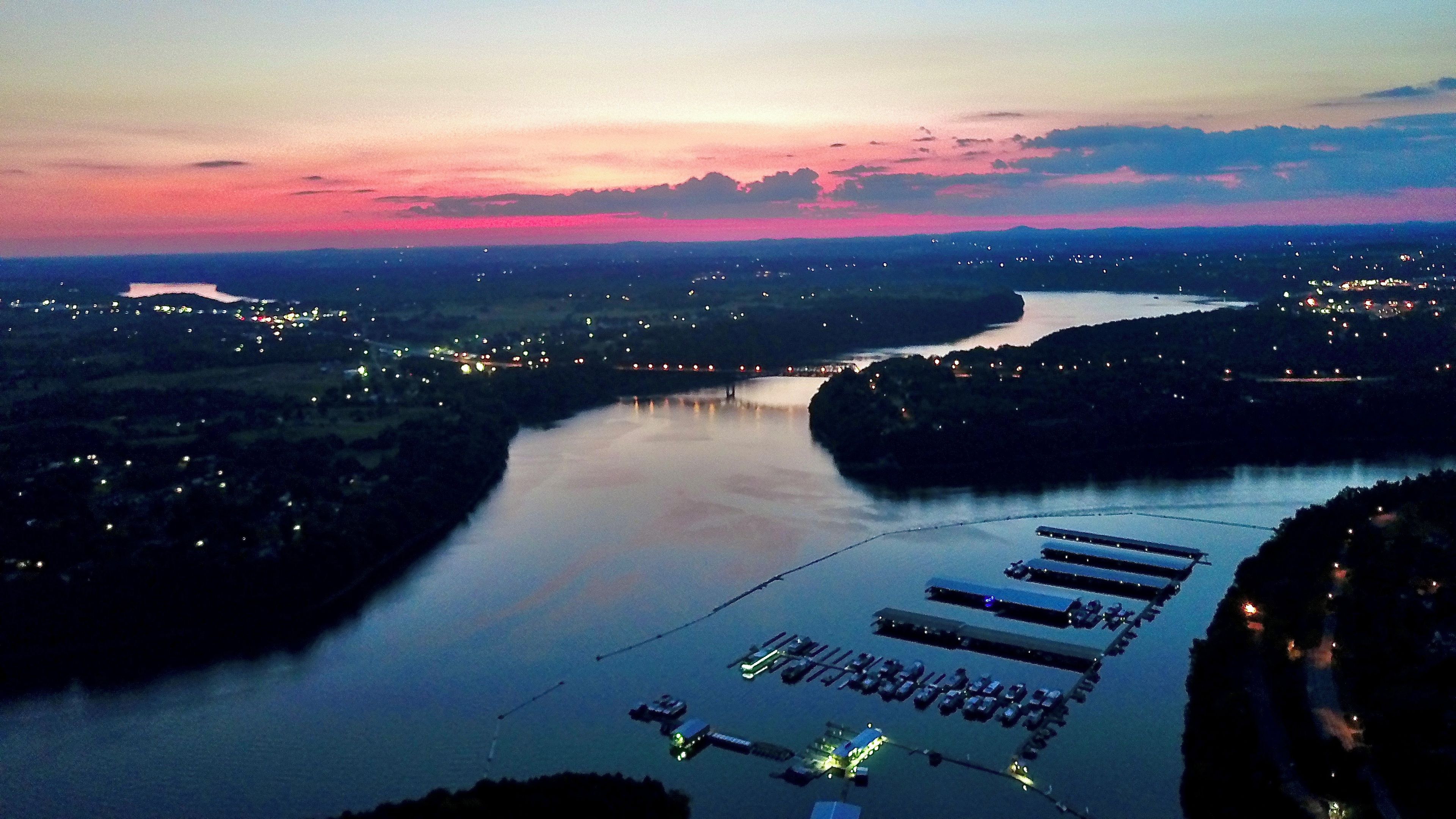 A river with a dock and boats, surrounded by a landscape with distant lights.