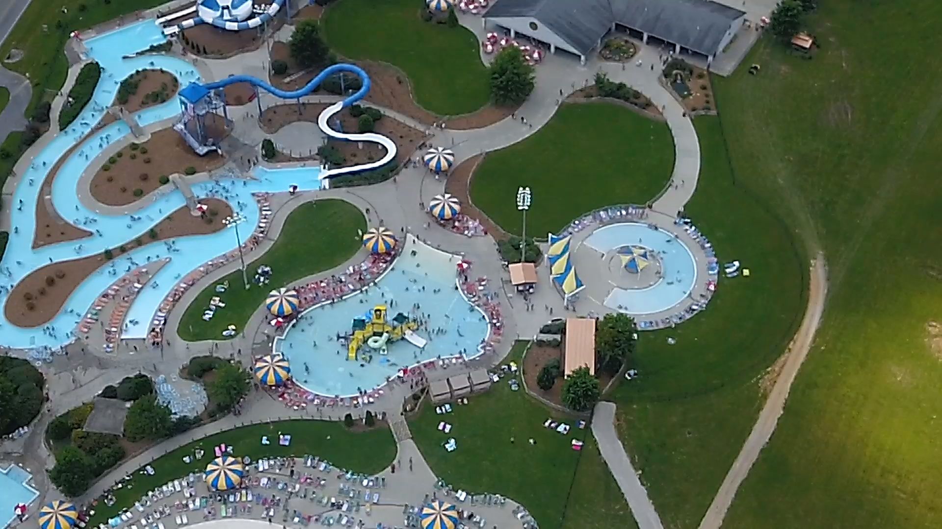 Vista aérea de un parque temático con diversas atracciones acuáticas, una plaza central y zonas verdes circundantes.