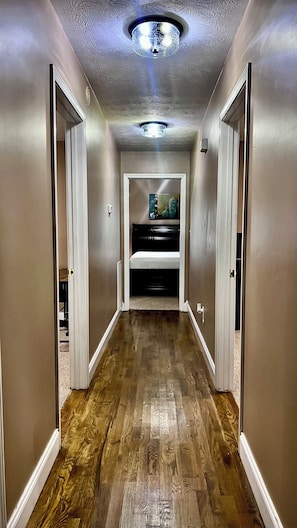 Un pasillo con piso de madera, una lámpara en el techo y una cama al fondo.