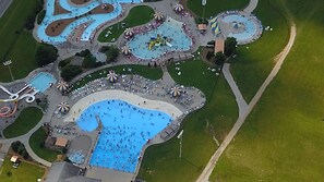 Vista aérea de un parque temático con varias atracciones acuáticas, incluyendo una piscina central grande y piscinas más pequeñas conectadas por pasarelas.