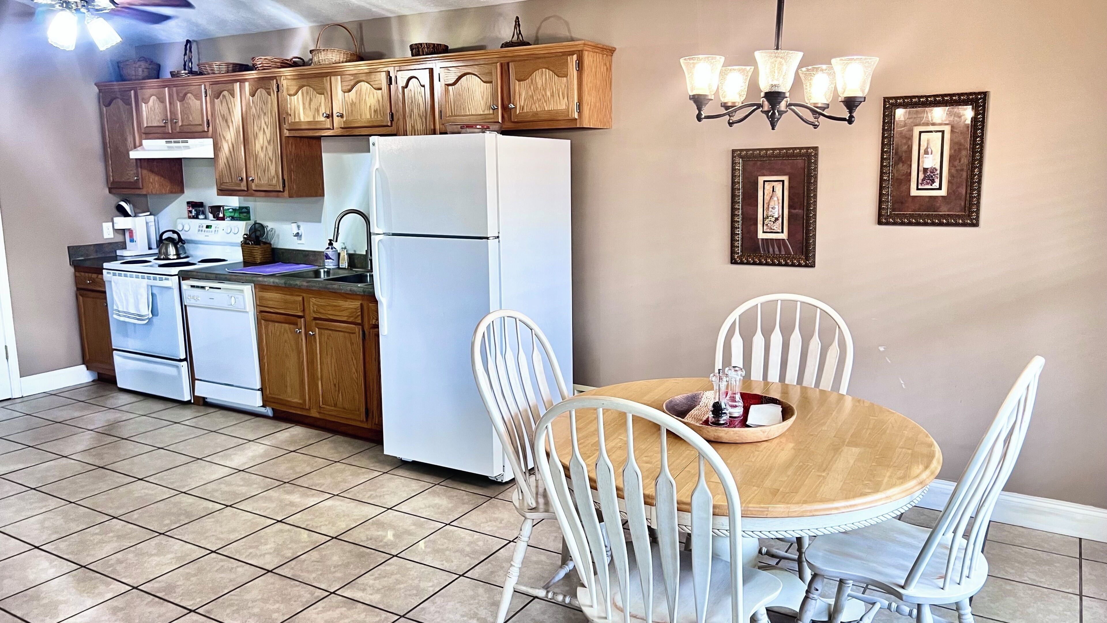 Una cocina con armarios de madera, un refrigerador blanco y una mesa de comedor con sillas blancas.