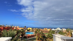 A coastal resort with a swimming pool, palm trees, and buildings with red and yellow facades. - Costa Adeje Sunset Ocean View Garden Studio B (Adeje)