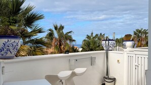 A balcony with a white table and chairs, a potted plant, and a view of palm trees and the sea. - Costa Adeje Sunset Ocean View Garden Studio B (Adeje)