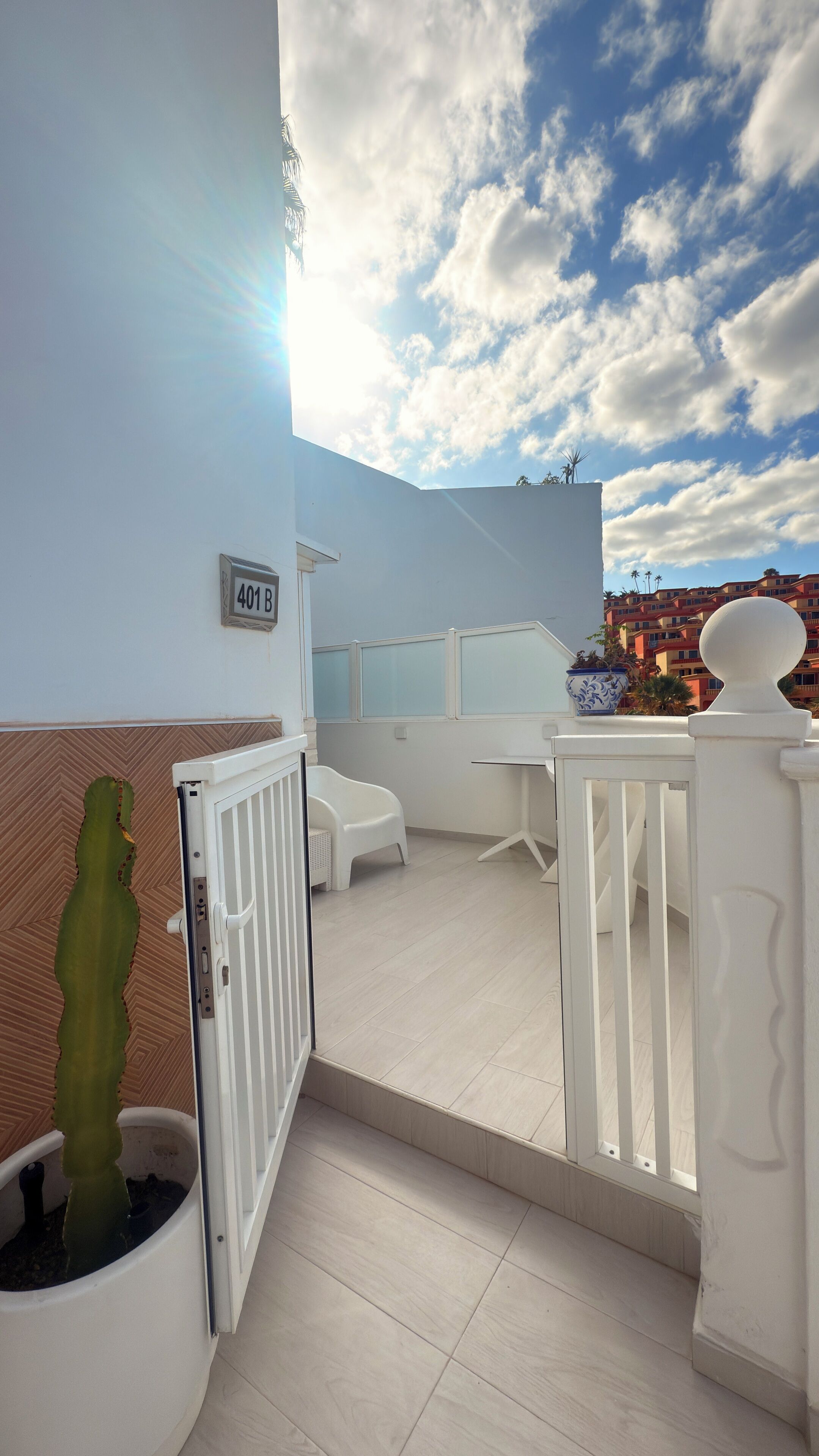 Ein Balkon mit weißer Brüstung, einem Topf mit Kaktee und einem kleinen Tisch.
