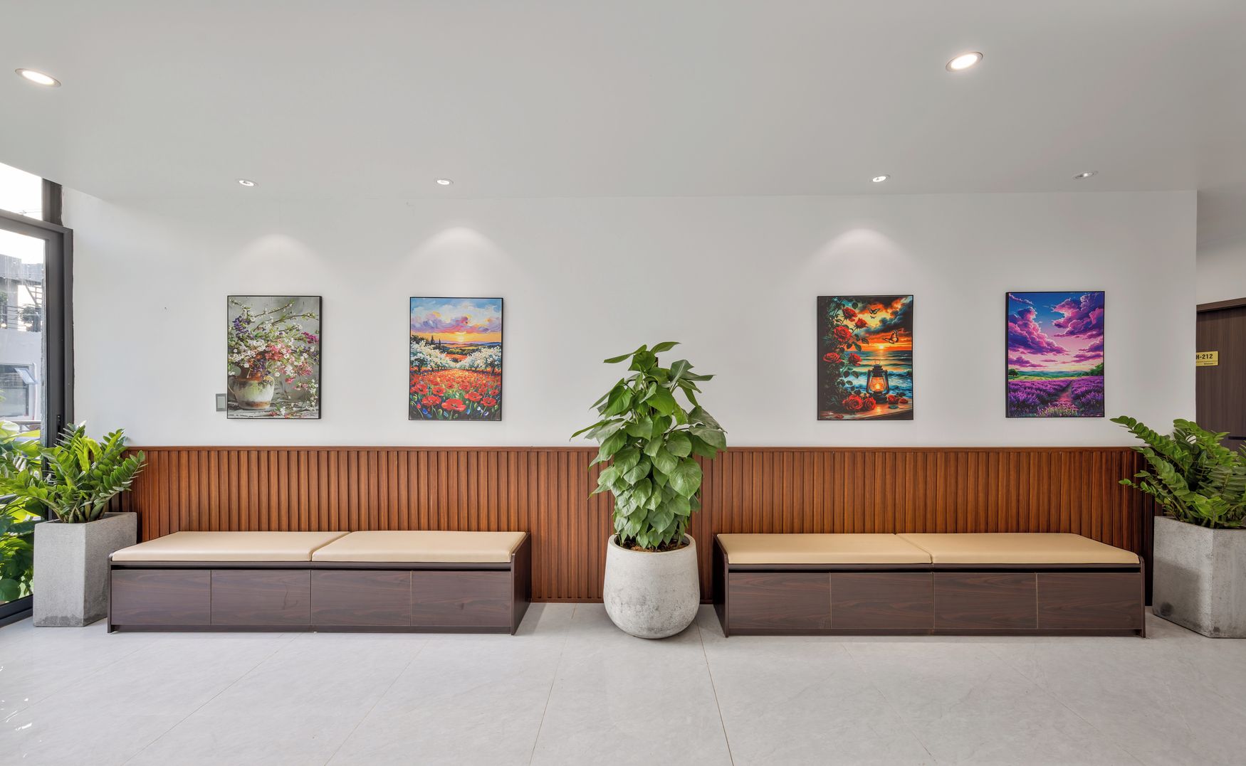 A reception area with two wooden benches, a large potted plant, and four framed artworks on the wall.