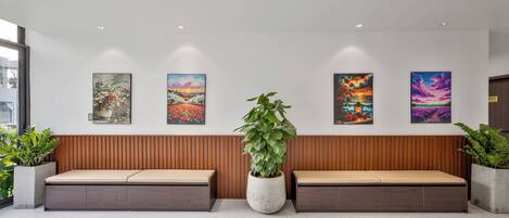 A reception area with two wooden benches, a large potted plant, and four framed artworks on the wall.