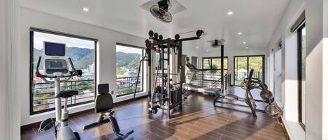 A spacious gym with various exercise equipment, large windows offering views of the outdoors, and a modern interior design.