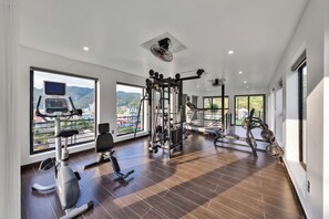 Een ruime fitnessruimte met diverse trainingsapparaten, grote ramen met uitzicht op het omliggende landschap, en een modern interieur.