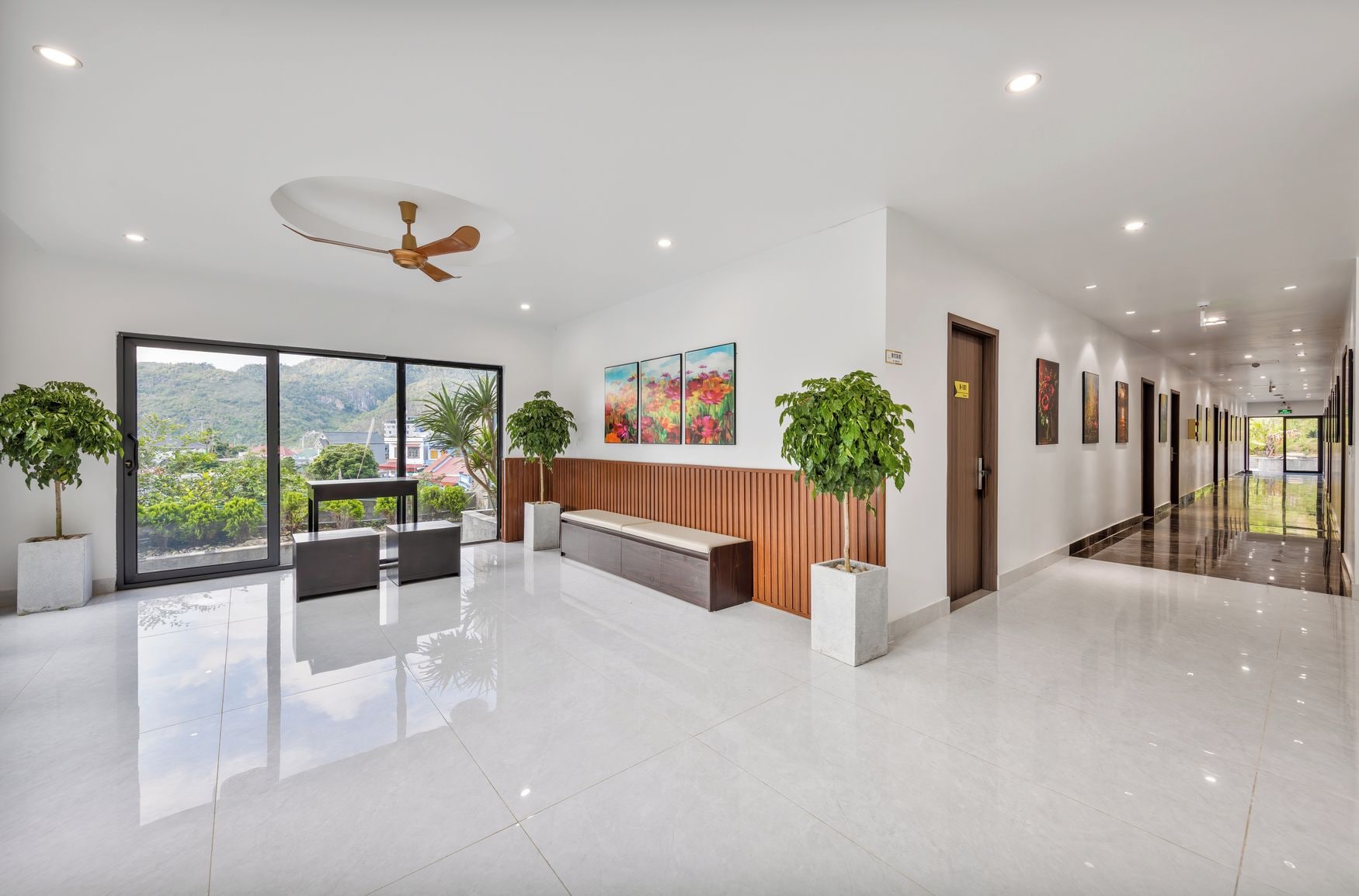 A modern lobby with a reception desk, seating area, and large windows offering a view of greenery and buildings.