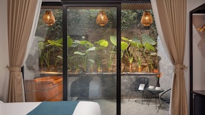 Een moderne hotelkamer met een grote schuifglazen deur die uitkomt op een buitenruimte met planten en een houten bankje.
