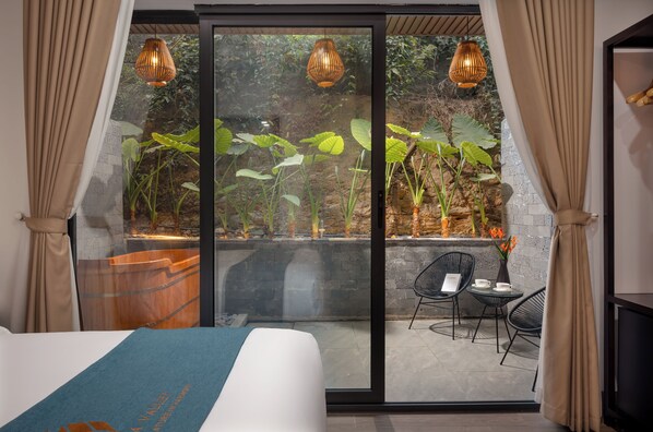 Een moderne hotelkamer met een grote schuifglazen deur die uitkomt op een buitenruimte met planten en een houten bankje.