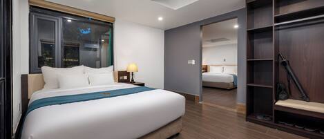 A modern hotel room with a large bed, a desk, a chair, a wardrobe, and a window with blinds.