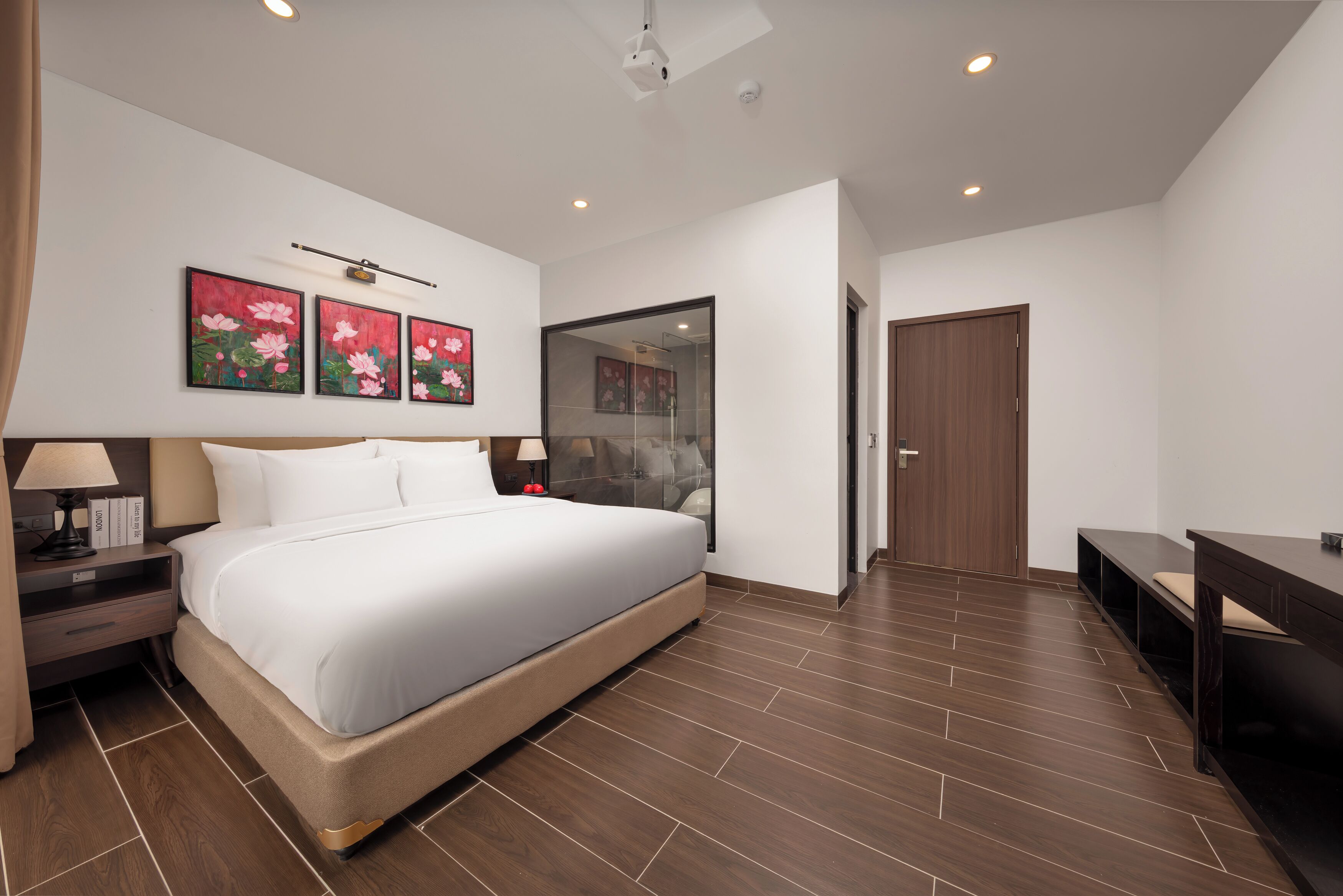 A modern hotel room with a large bed, bedside tables, a desk, and artwork on the wall.